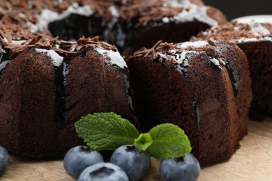 Photo of Delicious bundt cake with blueberries, mint and chocolate shavings on wooden table, closeup