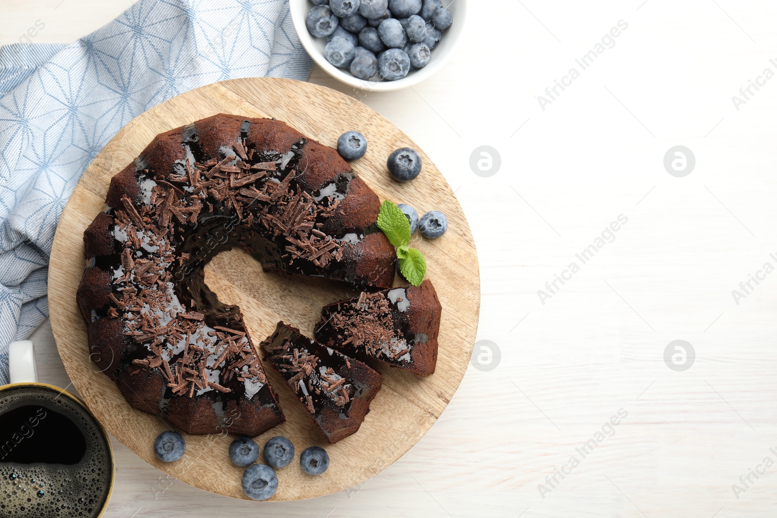 Delicious bundt cake with blueberries, mint, chocolate shavings and coffee on light wooden table, flat lay. Space for text Photo of Delicious bundt cake with blueberries, mint, chocolate shavings and coffee on light wooden table, flat lay. Space for text