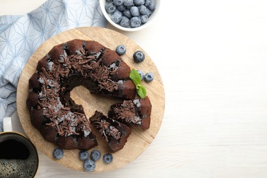 Photo of Delicious bundt cake with blueberries, mint, chocolate shavings and coffee on light wooden table, flat lay. Space for text