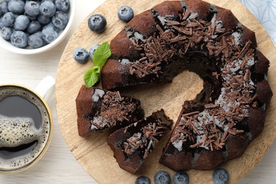 Photo of Delicious bundt cake with blueberries, mint, chocolate shavings and coffee on light wooden table, flat lay