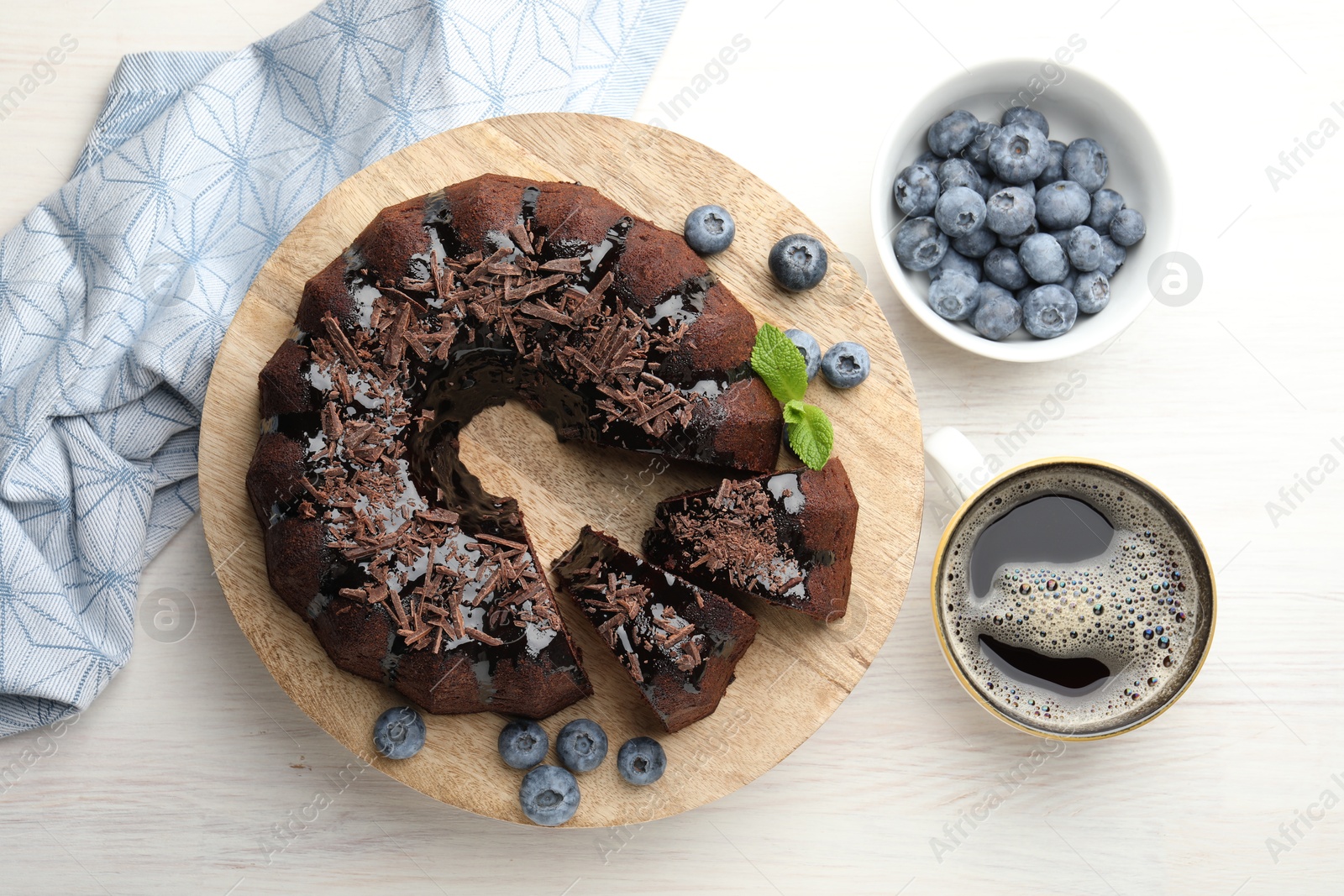 Delicious bundt cake with blueberries, mint, chocolate shavings and coffee on light wooden table, flat lay Photo of Delicious bundt cake with blueberries, mint, chocolate shavings and coffee on light wooden table, flat lay