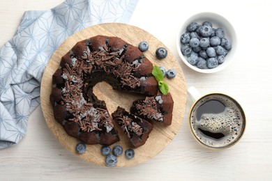 Photo of Delicious bundt cake with blueberries, mint, chocolate shavings and coffee on light wooden table, flat lay