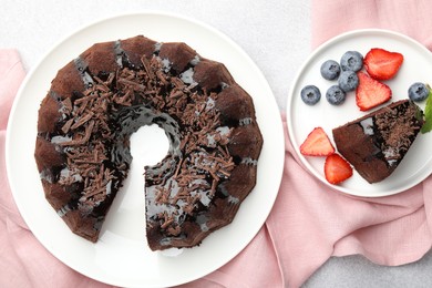 Photo of Delicious chocolate bundt cake with strawberries and blueberries on light grey textured table, flat lay