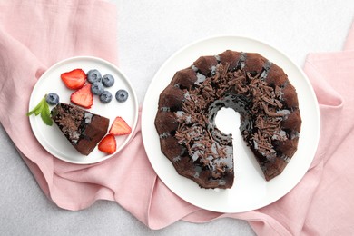Photo of Delicious chocolate bundt cake with strawberries and blueberries on light grey textured table, flat lay