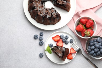 Photo of Delicious chocolate bundt cake with strawberries and blueberries on light grey textured table, flat lay. Space for text