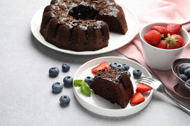 Photo of Delicious chocolate bundt cake with strawberries and blueberries on light grey textured table, closeup