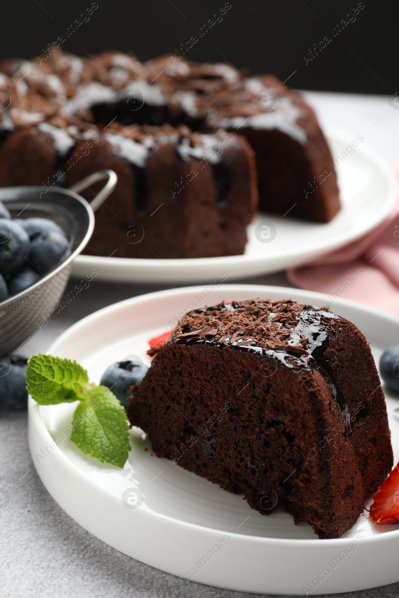 Piece of delicious chocolate bundt cake with mint and blueberries on light grey textured table against black background, closeup Photo of Piece of delicious chocolate bundt cake with mint and blueberries on light grey textured table against black background, closeup