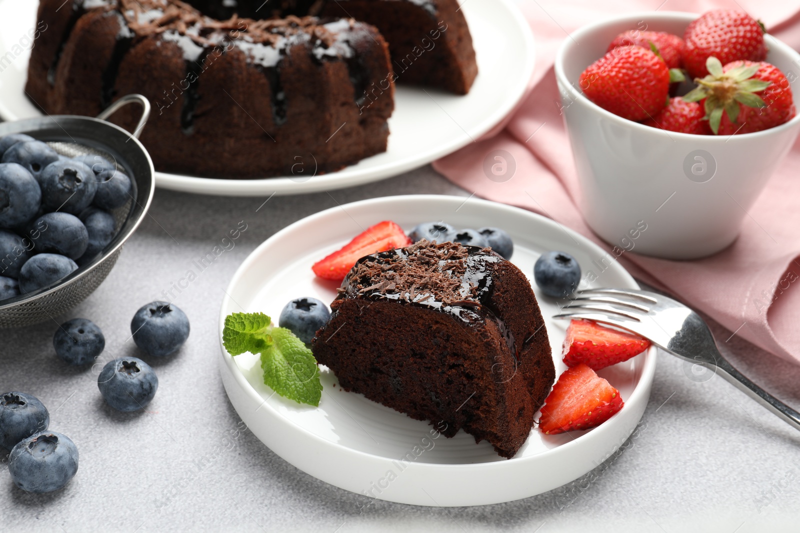 Piece of delicious chocolate bundt cake with strawberries, mint and blueberries on light grey textured table, closeup Photo of Piece of delicious chocolate bundt cake with strawberries, mint and blueberries on light grey textured table, closeup