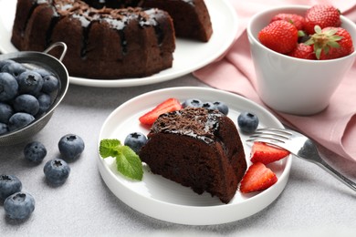 Photo of Piece of delicious chocolate bundt cake with strawberries, mint and blueberries on light grey textured table, closeup
