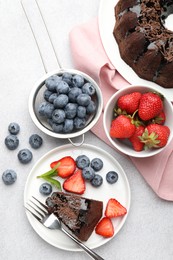 Photo of Delicious chocolate bundt cake with strawberries, mint and blueberries on light grey textured table, flat lay