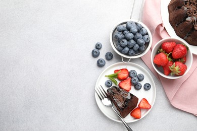 Photo of Delicious chocolate bundt cake with strawberries and blueberries on light grey textured table, flat lay. Space for text