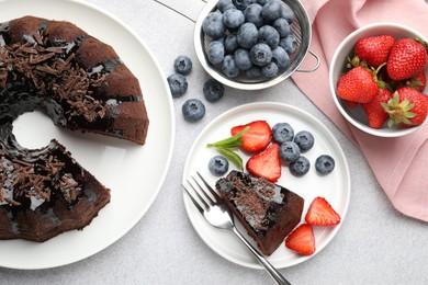 Photo of Delicious chocolate bundt cake with strawberries and blueberries on light grey textured table, flat lay