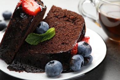 Photo of Pieces of delicious chocolate bundt cake with strawberries, mint and blueberries on grey table, closeup
