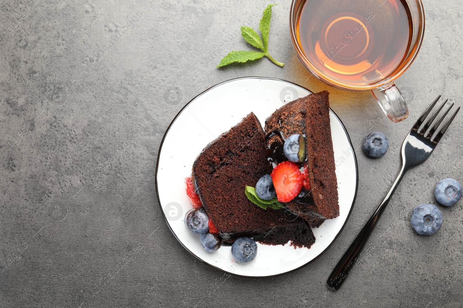 Pieces of delicious chocolate bundt cake with strawberries, mint and blueberries served on grey table, flat lay. Space for text Photo of Pieces of delicious chocolate bundt cake with strawberries, mint and blueberries served on grey table, flat lay. Space for text