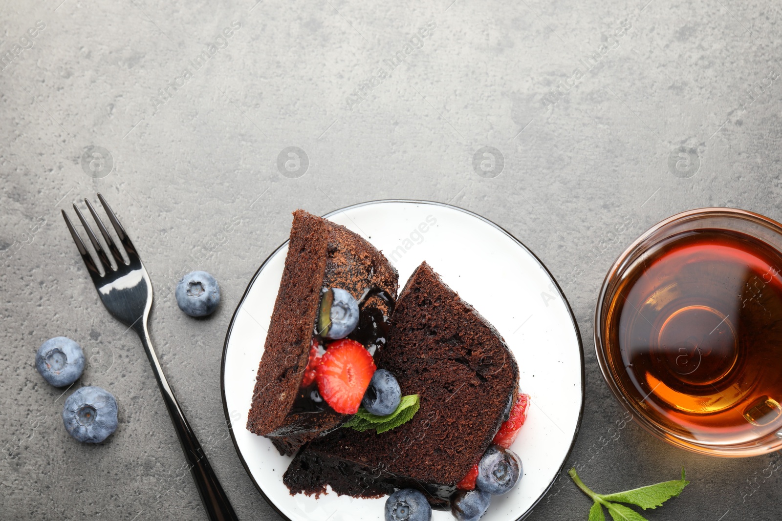 Pieces of delicious chocolate bundt cake with strawberries, mint and blueberries served on grey table, flat lay Photo of Pieces of delicious chocolate bundt cake with strawberries, mint and blueberries served on grey table, flat lay