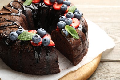 Photo of Delicious chocolate bundt cake with strawberries, mint and blueberries on wooden table, closeup