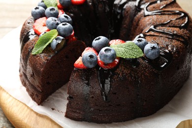 Photo of Delicious chocolate bundt cake with strawberries, mint and blueberries on table, closeup