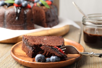 Photo of Piece of delicious chocolate bundt cake with blueberries on wooden table, closeup
