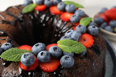 Photo of Delicious chocolate bundt cake with strawberries, mint and blueberries on table, closeup