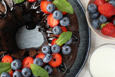 Photo of Delicious chocolate bundt cake with strawberries, mint and blueberries on light wooden table, flat lay