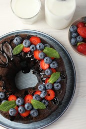 Photo of Delicious chocolate bundt cake with strawberries, mint and blueberries on light wooden table, flat lay