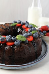 Photo of Delicious chocolate bundt cake with strawberries, mint and blueberries on light wooden table, closeup