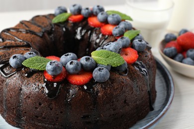 Photo of Delicious chocolate bundt cake with strawberries, mint and blueberries on light wooden table, closeup