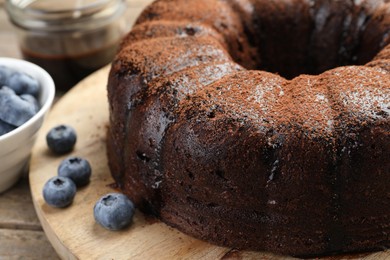 Photo of Delicious chocolate bundt cake with blueberries on wooden table, closeup