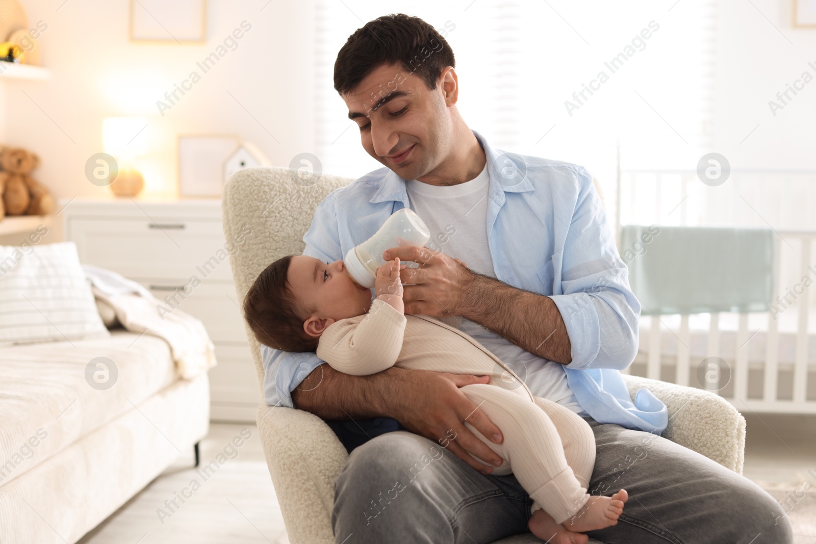 Father feeding his little baby with bottle on armchair at home Photo of Father feeding his little baby with bottle on armchair at home
