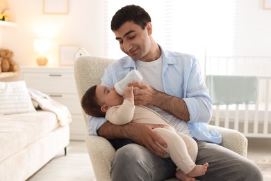 Photo of Father feeding his little baby with bottle on armchair at home