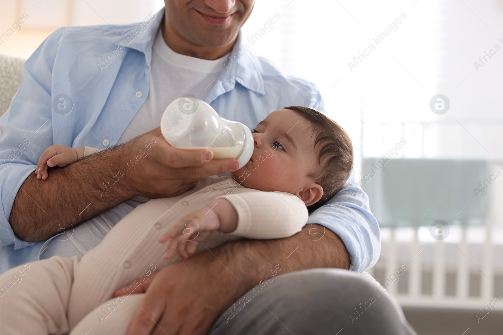 Father feeding his little baby with bottle on armchair at home, closeup Photo of Father feeding his little baby with bottle on armchair at home, closeup