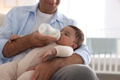 Photo of Father feeding his little baby with bottle on armchair at home, closeup