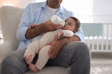 Photo of Father feeding his little baby with bottle on armchair at home, closeup