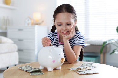 Photo of Girl putting her pocket money into piggybank at table indoors