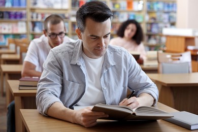 Photo of People studying at desks in public library, selective focus