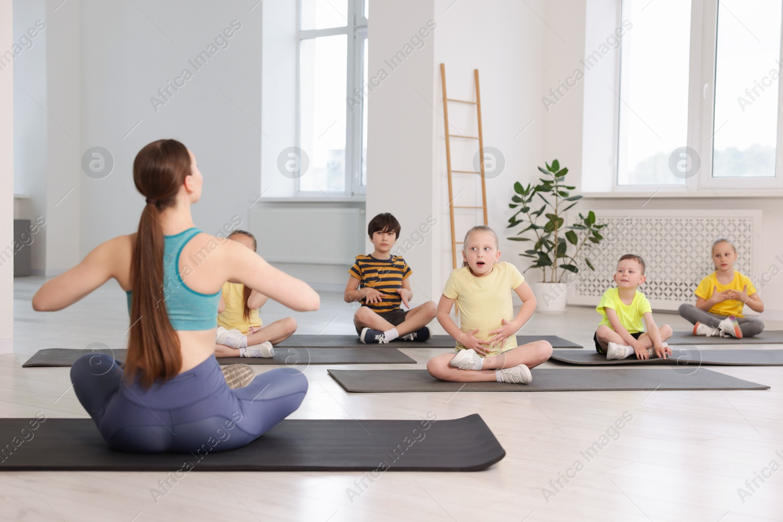 Group of children practicing yoga with coach on mats in class Photo of Group of children practicing yoga with coach on mats in class