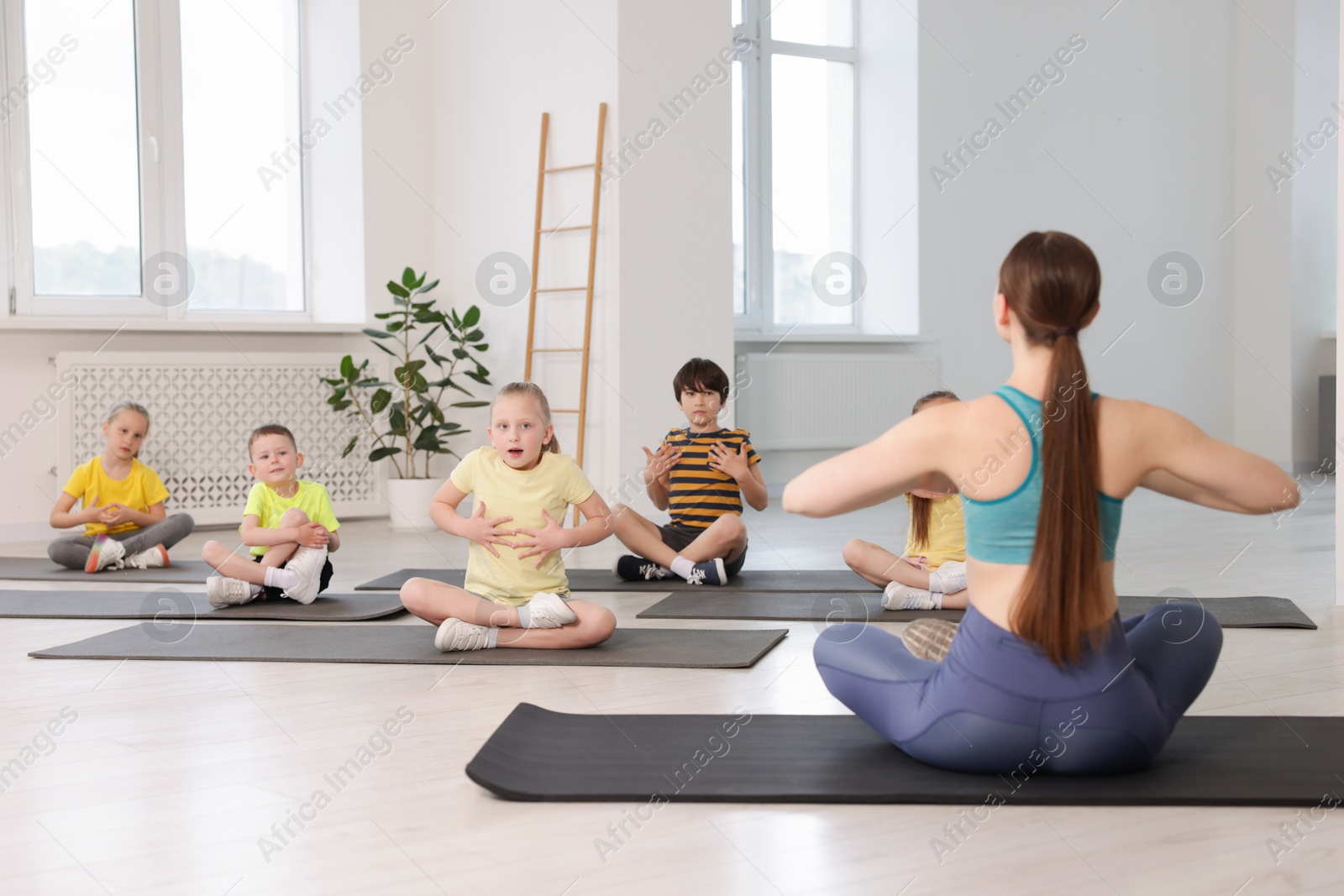 Group of children practicing yoga with coach on mats in class Photo of Group of children practicing yoga with coach on mats in class