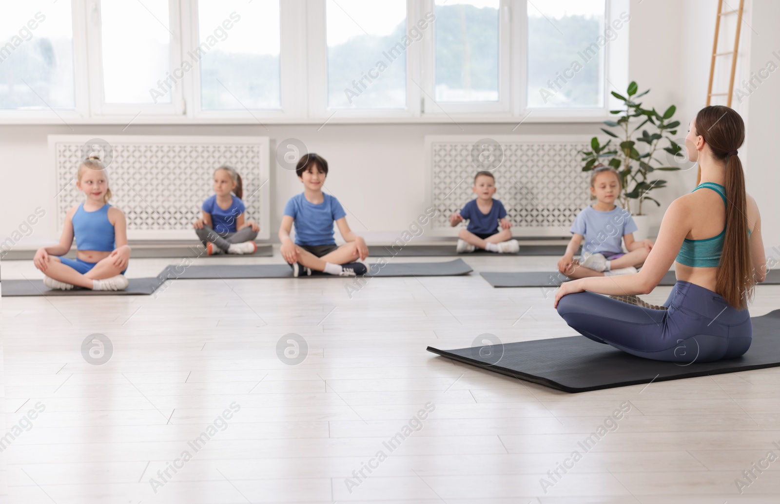 Group of children practicing yoga with coach on mats in class Photo of Group of children practicing yoga with coach on mats in class