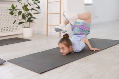 Photo of Cute girl practicing yoga on mat indoors