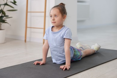 Photo of Cute girl practicing yoga on mat indoors