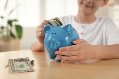 Photo of Boy putting pocket money into piggybank at table indoors, closeup