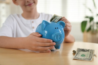 Photo of Boy putting pocket money into piggybank at table indoors, closeup