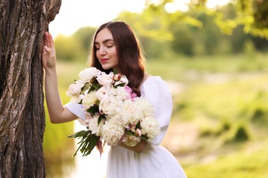 Photo of Beautiful woman with bouquet of peonies in park. Space for text