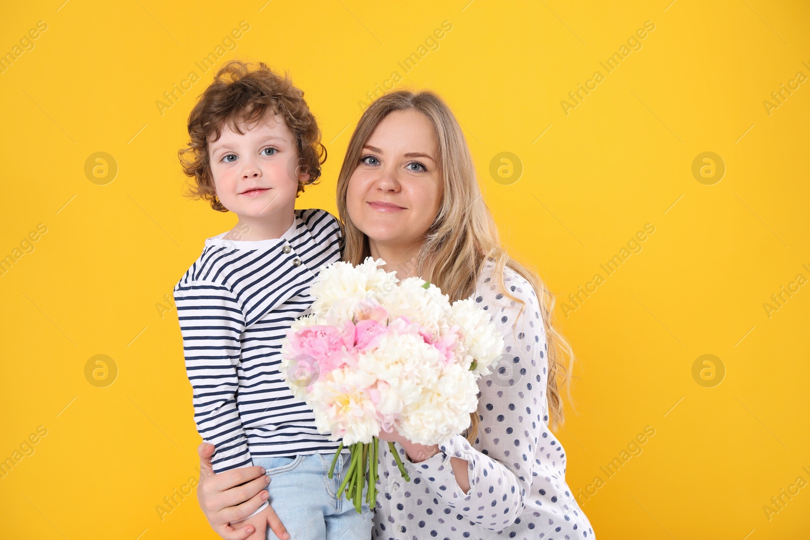 Little boy giving his mom beautiful peony flowers on yellow background Photo of Little boy giving his mom beautiful peony flowers on yellow background