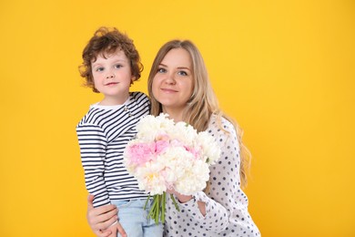 Photo of Little boy giving his mom beautiful peony flowers on yellow background