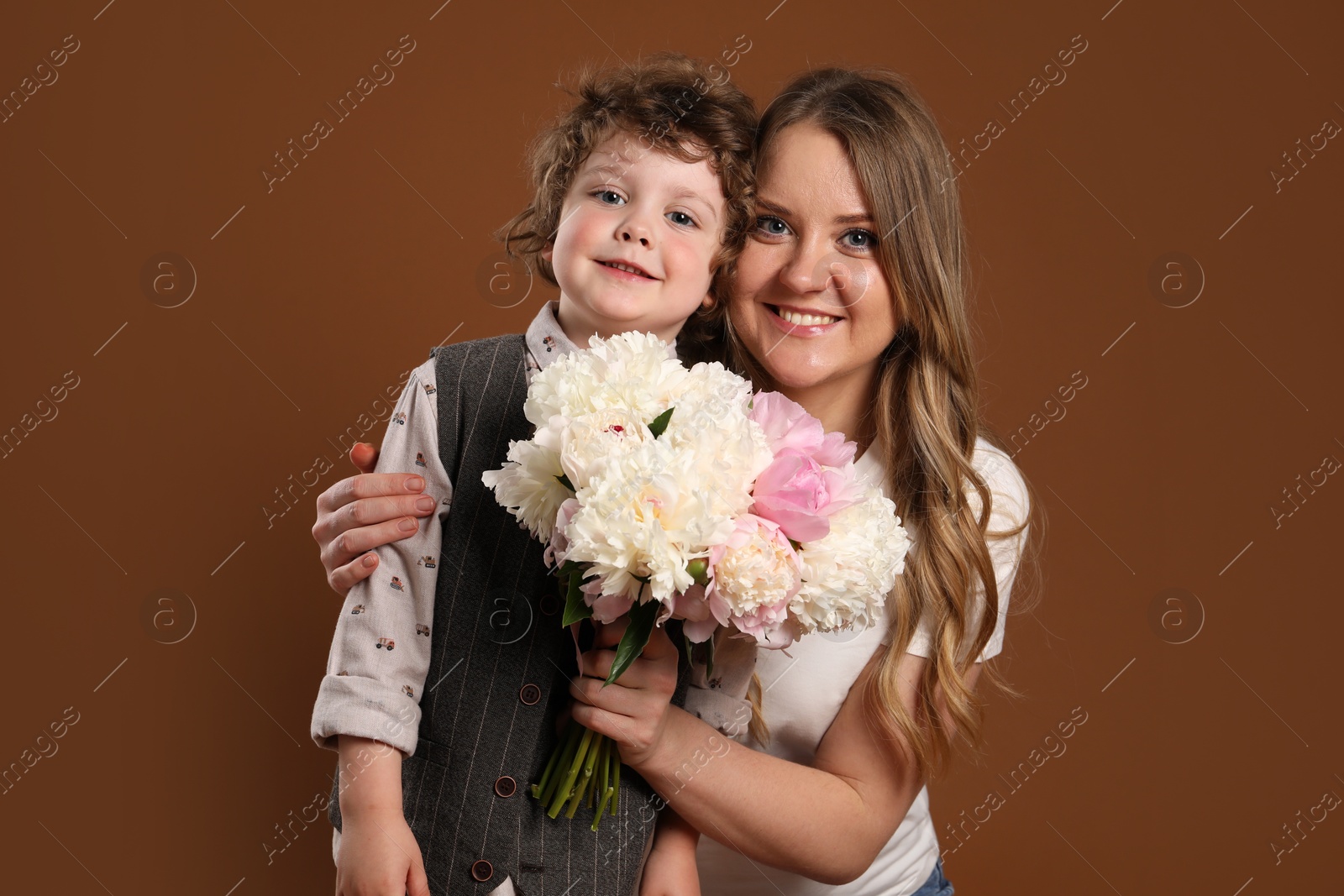 Little boy giving his mom beautiful peony flowers on brown background Photo of Little boy giving his mom beautiful peony flowers on brown background