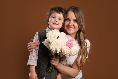 Photo of Little boy giving his mom beautiful peony flowers on brown background