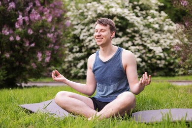 Photo of Young man practicing yoga on mat in park