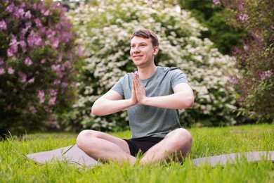 Photo of Young man practicing yoga on mat in park