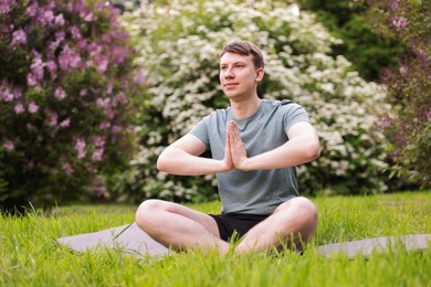 Photo of Young man practicing yoga on mat in park
